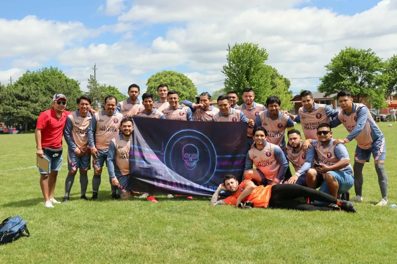 El equipo de La Calle Maldita posa en una cancha de pasto con su bandera del cráneo de neón